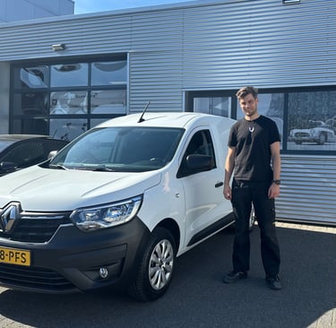 A man in a black t-shirt standing next to a white Renault Kangoo commercial van in front of an automotive building.