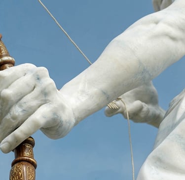Close-up of a marble statue's hand gripping a wooden bow against a clear blue sky.