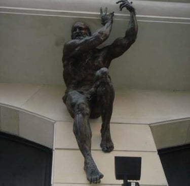 Bronze muscular male statue mounted to a stone wall as an architectural feature on a building facade.