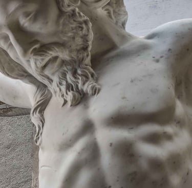 A close-up of a white marble religious sculpture showing the bearded face and torso of Jesus on the cross.