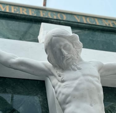 White marble Jesus Christ crucifixion statue on a cemetery headstone with Latin inscription.