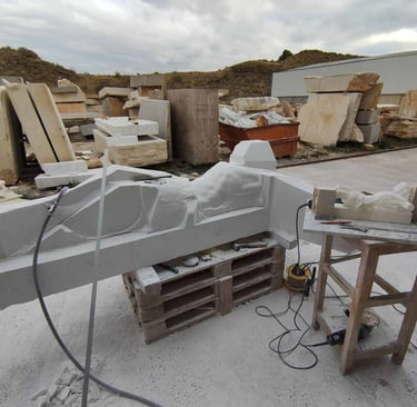 A stone sculpture in progress on a pallet in a masonry workshop with marble blocks and tools.