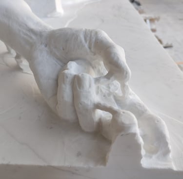Close-up of a hand being carved from a white marble block in a sculptor's workshop.