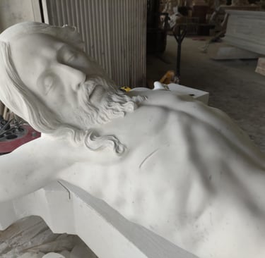 Hand-carved white marble statue of Jesus Christ on the cross inside a stone masonry workshop.