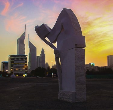 A stone sculpture stands against the Dubai skyline and Emirates Towers during a vibrant sunset.