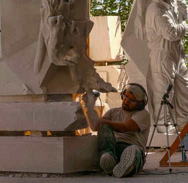 Professional sculptor using a power tool to carve intricate details into a large sandstone statue.