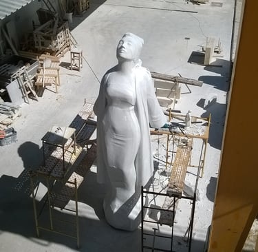 A large white marble statue of a standing woman inside a stone carving workshop with scaffolding.