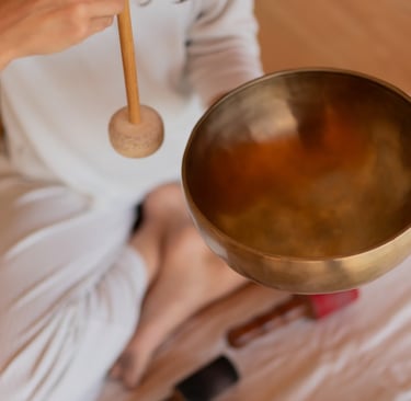 A person using a mallet to play a brass Tibetan singing bowl for sound healing and meditation.
