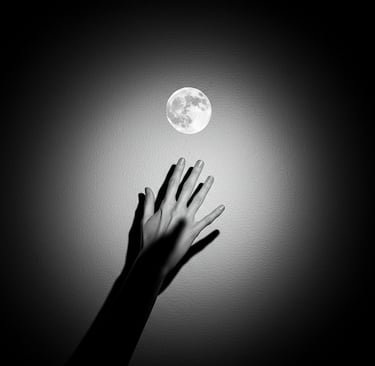 a hand reaching out for the moon in a black and white photograph