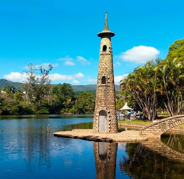 a clock tower in a park with a bridge over a river