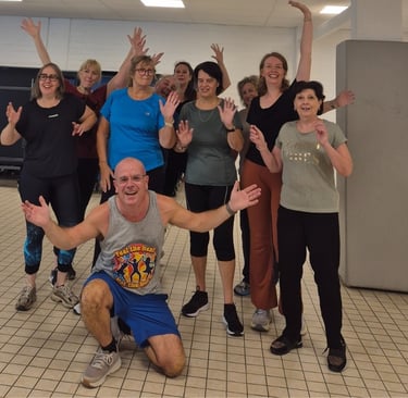 Group of smiling adults after a Groove Fitness disco class in Leuven, with Richard kneeling at the front, arms open