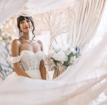 Ritratto emozionale di una sposa sorridente, avvolta da veli e luce soffusa, con bouquet chiaro.