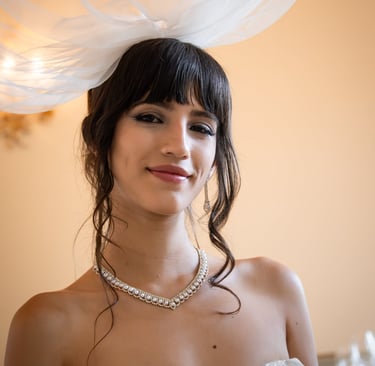 Primo piano elegante di una sposa con cappello di tulle e sorriso leggero, su sfondo caldo.