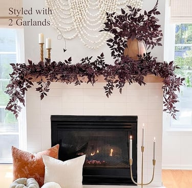 White fireplace mantel styled with two burgundy faux garlands, candles, and fall pillows