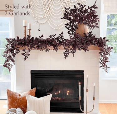 Fall fireplace decor with faux burgundy leaf garlands, cozy throw pillows, and taper candles