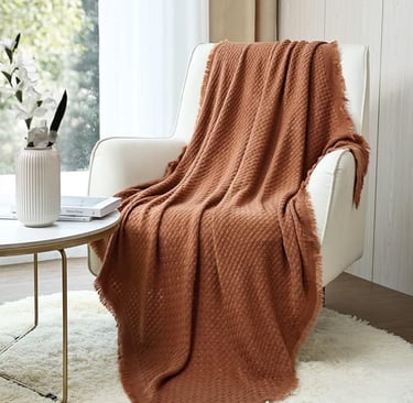 Rust-colored textured throw blanket draped over a white armchair in a modern, cozy living space
