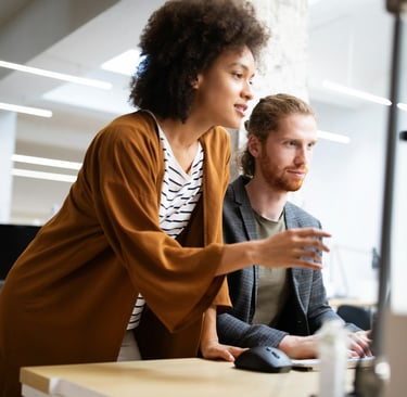 a woman in a brown sweater and a man in a gray jacket working in front of a computer