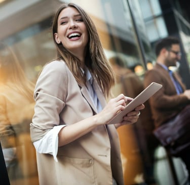 woman in a blazer and white shirt with rolled up sleeves. standing outside, holding a digital tablet