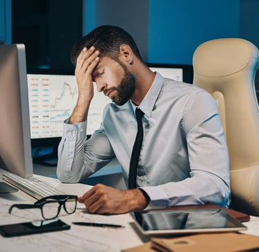 Stressed businessman sitting at his desk, holding his head in one hand
