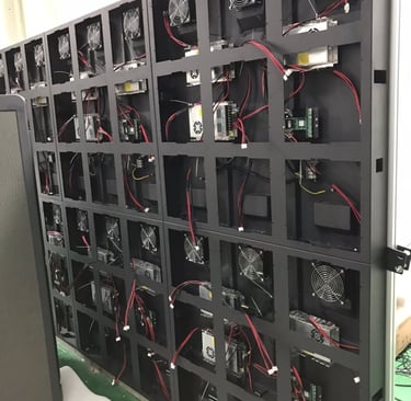 Rear view of an outdoor LED video wall display showing modular power supplies, cooling fans, and wiring.