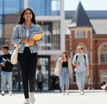 A young Pakistani student walking through a British university campus, exuding fresh, youthful energy in bright daylight.