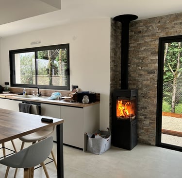 Poêle à bois moderne installé dans une cuisine contemporaine avec mur en pierre et baies vitrées