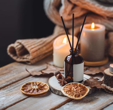 Cozy autumn flat lay with lit candles, amber glass reed diffuser, dried orange slices, star anise, a