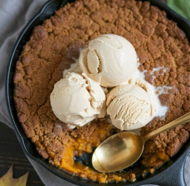 Warm pumpkin crisp topped with scoops of vanilla ice cream in a black skillet.