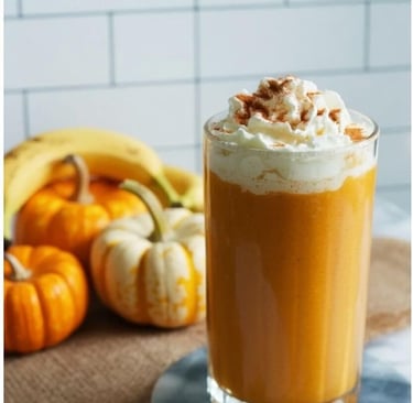 Tall glass of pumpkin smoothie topped with whipped cream and cinnamon, with fresh bananas and small