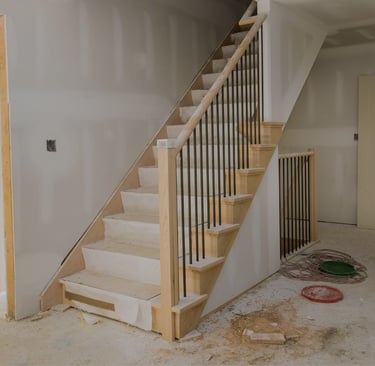 alt="Interior staircase surrounded by unfinished drywall and floor covering during home restoration"