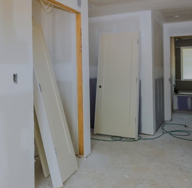alt="Room in mid-renovation with drywall, exposed outlets, and interior door leaning against wall"
