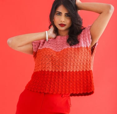 Woman wearing a handmade pink and red crochet shell stitch top against a bright red background.