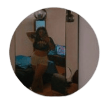 Woman taking a mirror selfie in a casual outfit standing in a dimly lit bedroom.