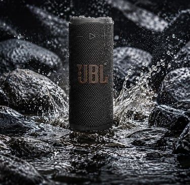 Enceinte JBL étanche noire avec gouttes d’eau, photo produit HDR ultra détaillée sur rochers mouillés.