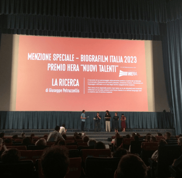 Biografilm Festival 2023 award ceremony for La Ricerca on a large cinema screen with speakers on stage.