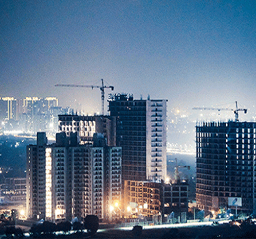 A city skyline at night featuring illuminated skyscrapers and buildings against a dark sky.