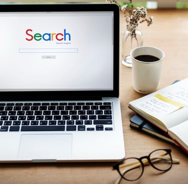 Imagem de um notebook com um site de buscas aberto e uma mesa com caderno