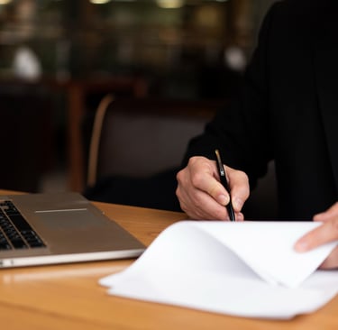 Advogado escrevendo em um papel em uma mesa com notebook