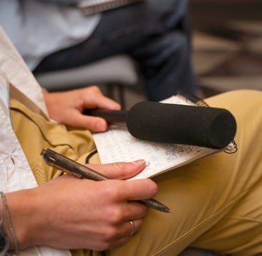 Pessoa sentada com um microfone e um bloco de anotações no colo