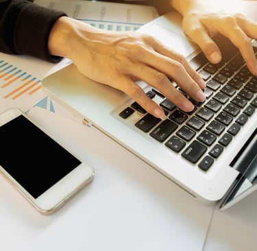 Mulher digitando em um notebook com um celular ao lado