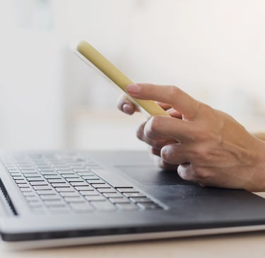 Notebook na mesa e mulher com celular na mão