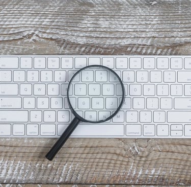 Teclado de computador e lupa em cima de mesa de madeira