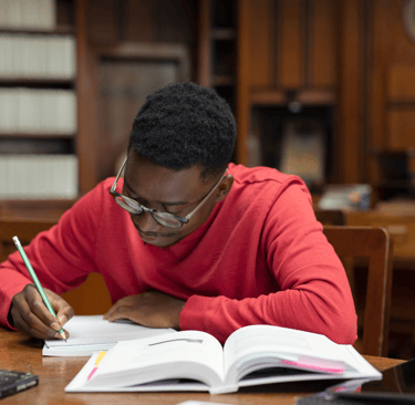 Un jeune homme écrivant dans un carnet tout en étudiant un livre ouvert, symbolisant réflexion