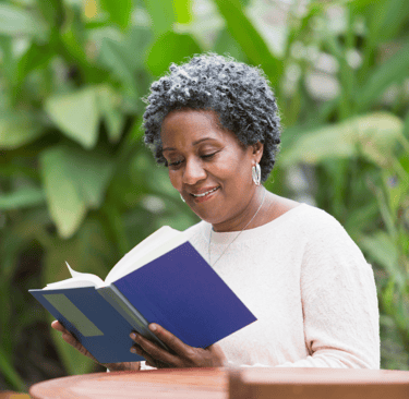Une femme souriante lisant un livre bleu dans un jardin verdoyant, symbolisant la paix.