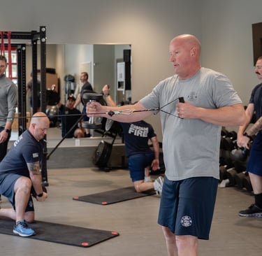 Firefighters performing strength training and cable machine exercises at a gym for physical fitness.