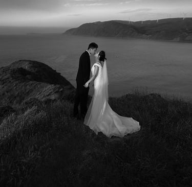 a bride and groom standing on a cliff overlooking the ocean