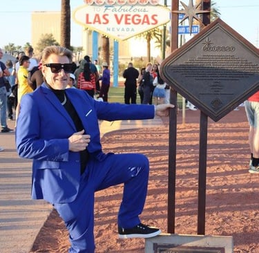 Tim in a blue suit poses by a bronze plaque near the Welcome to Fabulous Las Vegas sign.