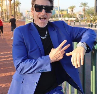 Tim in a vibrant blue suit and oversized sunglasses posing with a peace sign outdoors.