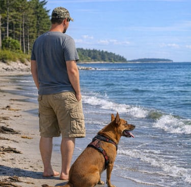 A man and his brown dog standing on a sandy beach looking at the blue ocean waves.