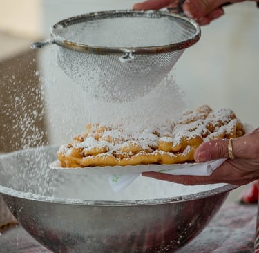 a funnel cake being dusted with powdered sugar